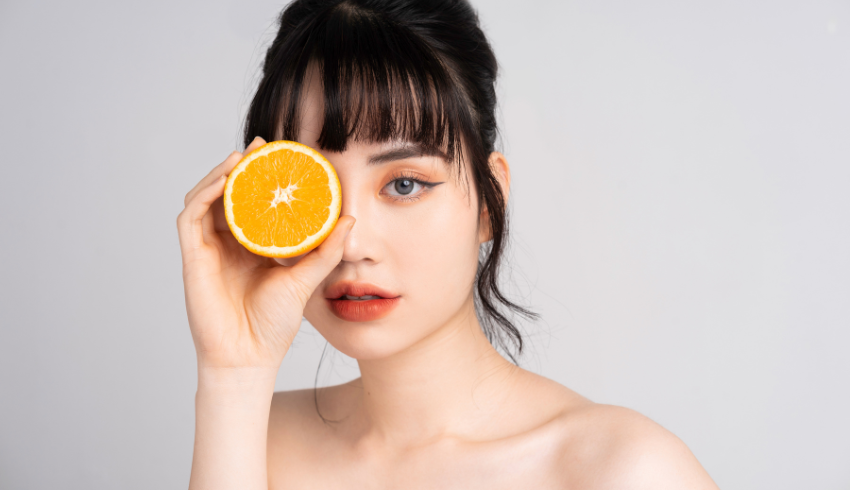 A woman holding half an orange over one eye.